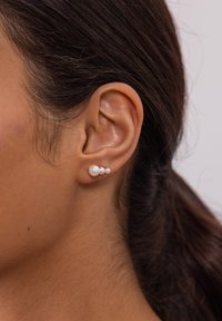 Drei Perlenohrringe mit einer goldenen Rückseite, die unterschiedliche Perlengrößen aufweisen: eine große und zwei kleinere. Glatte Textur, klassisches Design.