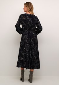 Långärmad svart klänning med ljusa blommönster, utsv�ängd kjol och rynkad detalj bak, i kombination med texturerade silverfärgade högklackade stövlar.