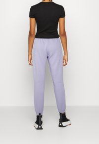 Svart, åtsittande kortärmad t-shirt i kombination med lila sweatpants, som har elastiska manschetter och en avslappnad passform, bärs med svarta snörboots.