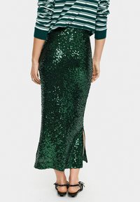 Green sequin skirt with a fitted design, featuring side slits and a slight shimmer. Back view shows texture and length to the mid-calf.