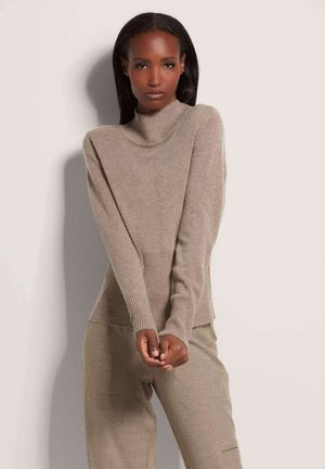 Beiger Strickpullover mit Trichterkragen, gerippten Bündchen und strukturiertem Körper. Kombiniert mit beigen, locker sitzenden Hosen. Weiches, warmes Material.