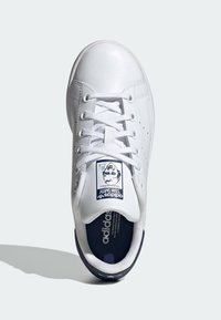 Sneaker Adidas Stan Smith bianca con lacci bianchi, interno blu navy e un ritratto sull'etichetta della lingua, vista dall'alto.