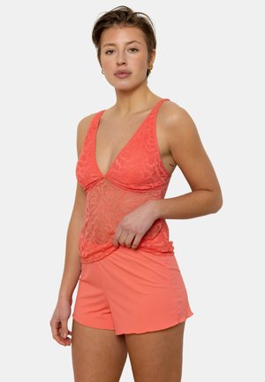 Haut en dentelle corail avec un design en V profond, superposé sur un short corail à côtes. Le haut présente une texture en dentelle transparente, créant un look délicat.
