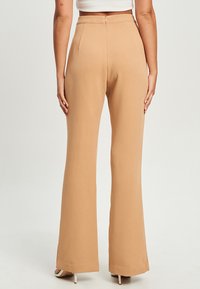 Beige uitlopende broek van gladde stof met een middelhoge taille, voorzien van een verborgen rits en een getailleerde pasvorm.