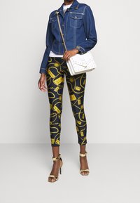 Jeansjacka med tryckknappar, svarta leggings med ett guldchain-mönster och guldremmar på klackarna. Vit handväska med nitar.