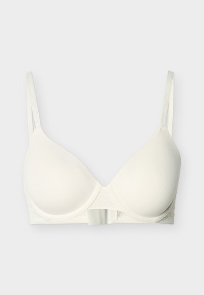 Λευκό μαξιλαρωτό σουτιέν με ρυθμιζόμενους ιμάντες και κούμπωμα μπροστά σε ανοιχτό φόντο.