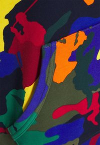 Färgglad camouflage-tröja med livliga mönster i röd, gul, grön, lila och orange, med en mjuk textur och en framficka.