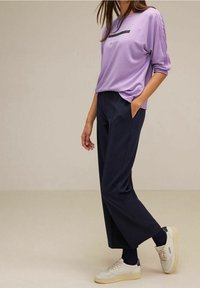 Lila långärmad skjorta med logotypdetalj, ihop med mörkblå byxor och vita sneakers. Mjuk tyg med avslappnad passform.