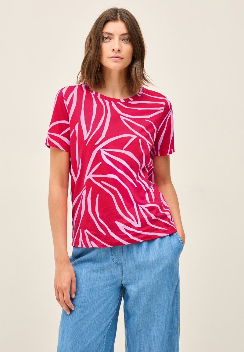 T-shirt in cotone rosso con motivi a foglia rosa, maniche corte e scollatura rotonda, abbinato a pantaloni a gamba larga blu chiaro.