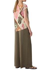 Kurzärmelige Bluse mit floralem Muster in Pink, Orange und Grün; kombiniert mit lockeren, olivgrünen Hosen und schwarzen Sandalen.