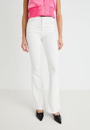 White flared jeans made of denim, featuring a fitted waist and straight cut through the leg, paired with black pointed shoes.