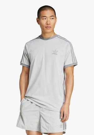 T-shirt atletica grigio chiaro con maniche corte, design raglan, scollatura rotonda e sottili dettagli a tre strisce sulle spalle.