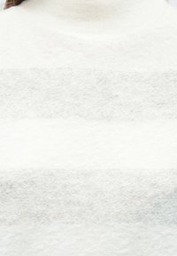 Pulover cu guler înalt de culoare deschisă, realizat dintr-o țesătură tricotată moale și texturată, cu dungi orizontale în nuanțe variate de alb și gri.