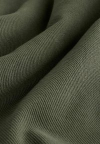 Artimųjų planų tekstūruota alyvuogių žalia medžiaga su matomomis smulkiomis raibutėmis ir minkštais raukšlėmis, sukuriančiomis šešėlius ir gilumą.