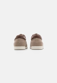 Zapatillas de tela y cuero en color marrón, con un perfil bajo, suela acolchada y diseño de cordones. Acabado texturizado en la parte superior.