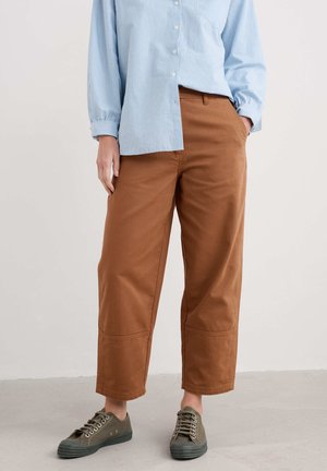 Bruine, wijde broek met een gladde textuur, voorzien van zijzakken en een gestikte zoom, gedragen met olijfgroene canvas sneakers.