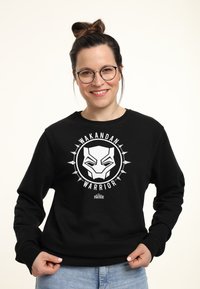 Czarna bluza z kapturem z białym graficznym wzorem przedstawiającym logo Czarnej Pantery oraz tekstem "WAKANDAN WARRIOR" w okrągłym układzie.