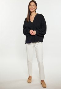 Černá blůzka s V-výstřihem a balónovými rukávy, s plisovaným lemem, nošena s bílými slim-fit kalhotami a béžovými slip-on botami s detaily.