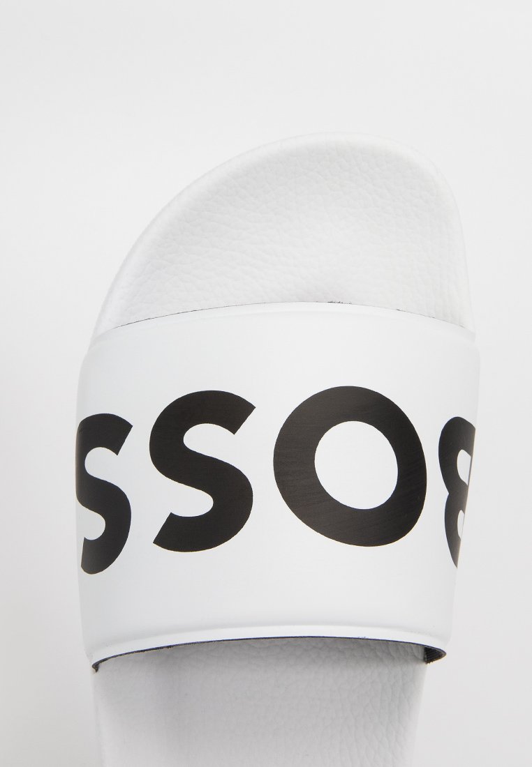 Sandale blanche à glissière avec des lettres noires partielles "SSOS" sur la sangle et un coussin de pied texturé, vue de dessus.