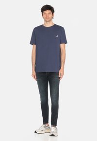 T-shirt a maniche corte blu navy con taschino, realizzato in cotone. Abbinato a jeans in denim scuri e sneakers chiare.