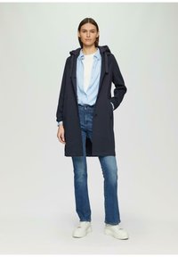 Cappotto con cappuccio di un blu scuro, con chiusura a bottone, indossato sopra una camicia azzurro chiaro e jeans. Presenta una vestibilità comoda e tasche. Sneakers bianche completano il look.