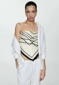 Top crema senza spalline con linee geometriche nere, abbinato a una camicia bianca ampia e pantaloni bianchi, che enfatizzano un design contemporaneo.