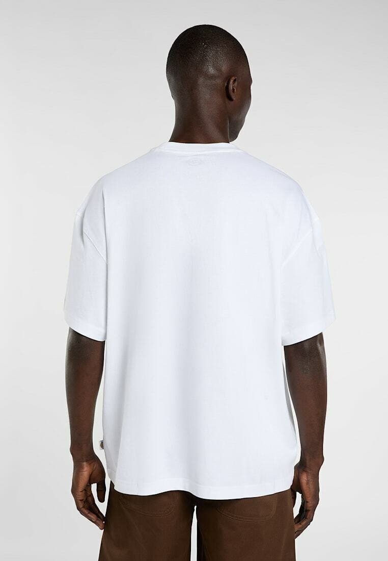 Mann mit dunkler Haut, der ein schlichtes weißes, übergroßes T-Shirt mit kurzen Ärmeln und braune Hosen trägt, von hinten vor grauem Hintergrund gesehen.