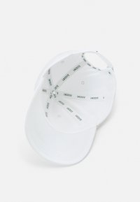 Gorra de béisbol blanca con visera curva. El interior presenta un patrón de logotipos repetidos en verde sobre un forro limpio y suave.