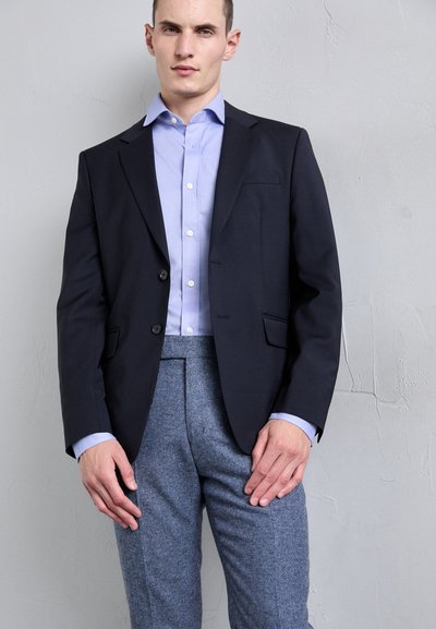 Sacou bleumarin cu două nasturi, buzunar pe piept, asortat cu o cămașă button-up albastră deschis; pantaloni texturați gri.