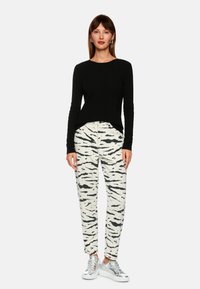 Black long-sleeve knit top paired with cream tapered pants featuring a black abstract pattern and silver sneakers. Simple modern design.