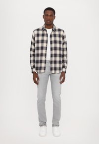 Svart och vit rutiga flanellskjorta, knäppning framtill, bärs över en vit t-shirt. Matchas med ljusgrå jeans och vita sneakers.