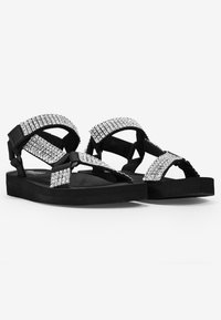 Sandalias de plataforma negras con correas adornadas con rhinestones, que presentan una suela plana texturizada y un diseño entrelazado para un ajuste seguro.