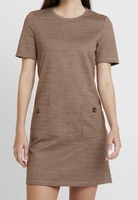 Robe marron à manches courtes avec un motif à carreaux, dotée d'un col rond et de deux poches avant ornées de boutons.