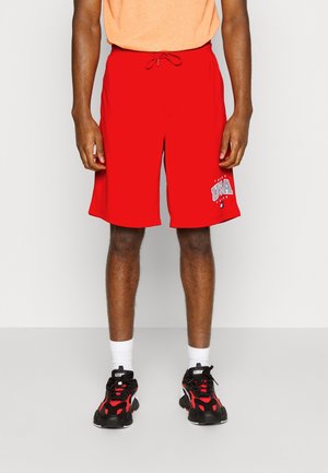 Red athletic shorts with an elastic waistband and drawstring, featuring a graphic print. Paired with black and red sneakers.