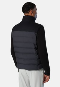 Gepolsterte Weste mit einem schwarzen oberen Bereich und einem grauen, gesteppte unteren Abschnitt. Verfügt über gerippte schwarze Ärmel und einen hohen Kragen.