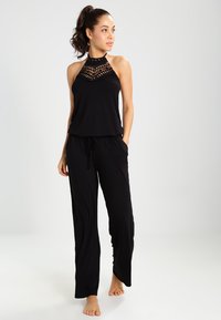 Schwarzer Jumpsuit mit einem Halterhalsdesign, gemustertem Oberteil, lockerer Passform und Kordelzug in der Taille; leichtes Material.