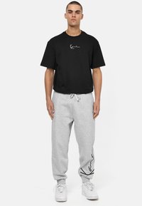 Black cotton t-shirt with short sleeves and white logo. Gray sweatpants with elastic waistband and black line design on the side.