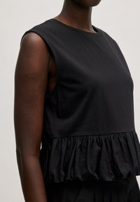 Schwarzes Baumwolloberteil mit rundem Ausschnitt, ärmellosem Design und volants Saum. Glatte Textur mit lockerer Passform.