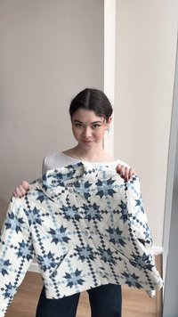 Tânără cu păr închis la culoare ținând o jachetă albă matlasată cu modele de stele albastre, stând în interior, în fața unui perete bej.