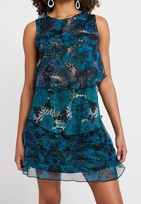 Vestido sin mangas en tono azul aguamarina con diseño en capas; presenta patrones florales, textura transparente y una silueta fluida. Acentuado con detalles en negro.