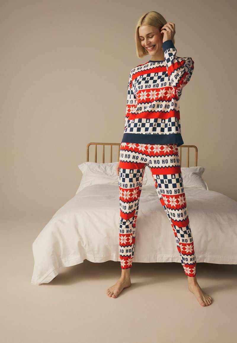 Punat ja siniset kuvioidut pyjamapuvut, joissa on "HO HO" -teksti, lumihiutaleita ja ruutukuvioita. Pehmeä kangas ja rento istuvuus.