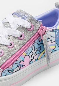 Baskets en toile argentée pailletée avec des motifs colorés d'ailes et de cœurs, des lacets blancs, des accents roses et une fermeture éclair sur le côté.