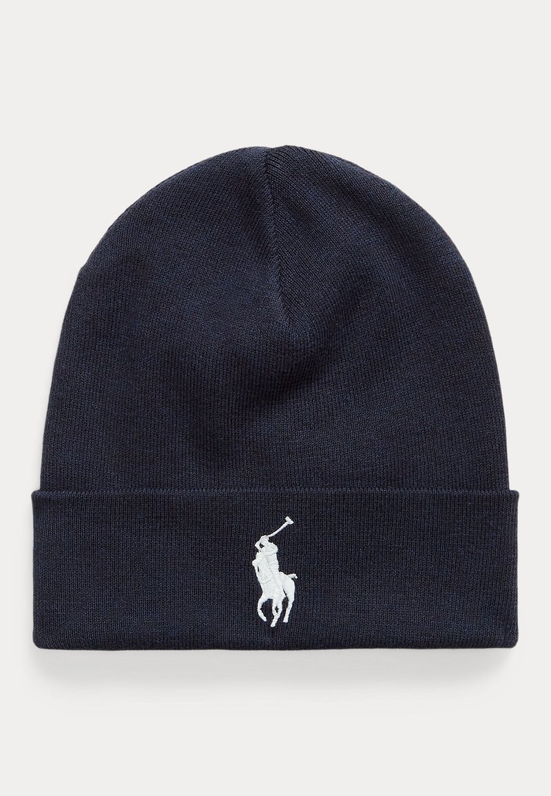 Tumša zila adīta cepure, kas izgatavota no mīksta materiāla, ar balto izšūto polo logotipu priekšpusē un salocītu maliņu dizainu.
