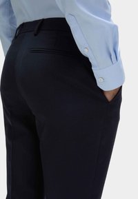 Czarne eleganckie spodnie o gładkiej fakturze, z bocznymi kieszeniami i delikatnym akcentem tylnej kieszeni. W zestawieniu z jasnoniebieską koszulą.