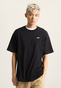 Černé tričko s krátkým ruk�ávem vyrobené z bavlny, s malým bílým potiskem na hrudi a klasickým kulatým výstřihem. Hladká textura.