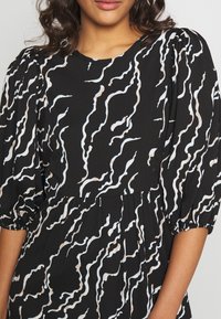 Svart klänning med ett vågigt vitt och beige abstrakt mönster, puffade kortärmar och en rynkad midja för en avslappnad passform.