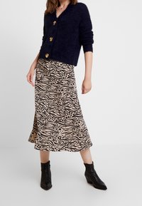 Navy fluffy cardigan with gold buttons paired with a beige skirt featuring a black animal print design and high-heeled black ankle boots.