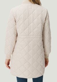 Cappotto lungo beige trapuntato con polsini a costine e scollatura rotonda, caratterizzato da un motivo a diamante e una vestibilità rilassata.
