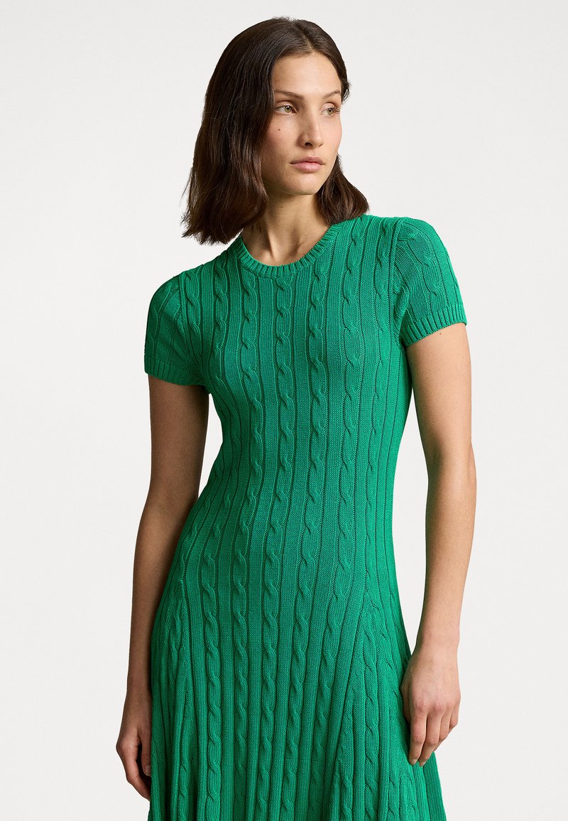 Vestido de punto verde con mangas cortas, que cuenta con un patrón de cable texturizado y un corsé ajustado que se ensancha en la cintura.