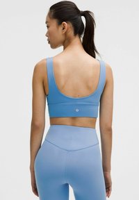 Hele sinise sportliku lõikega crop-top, millel on laiade sangadega ja sile tekstuur, koos kõrge vöökohtadega retuusidega samas värvitoonis ja disainiga.